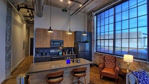 A modern kitchen with a central island, bar stools, a leather armchair, and a large window. - Chic Ultramodern Loft Suite w/ Designer Features (St. Louis)