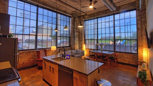 A kitchen with large windows, a central island, and a dining area with chairs and a table. - Chic Ultramodern Loft Suite w/ Designer Features (St. Louis)