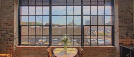 A room with a large window, a table with chairs, and a vase with flowers.