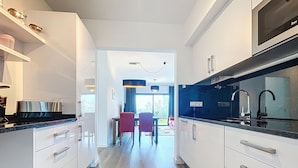 Una cocina moderna con armarios blancos, encimera negra y comedor con sillas rojas.