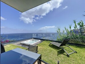A balcony with a hot tub, a table, and chairs overlooking the ocean.