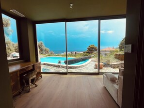 A room with a large sliding glass door leading to a pool area with a view of the sea.