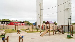 A playground with various play structures, including a slide and swings, surrounded by a fence.