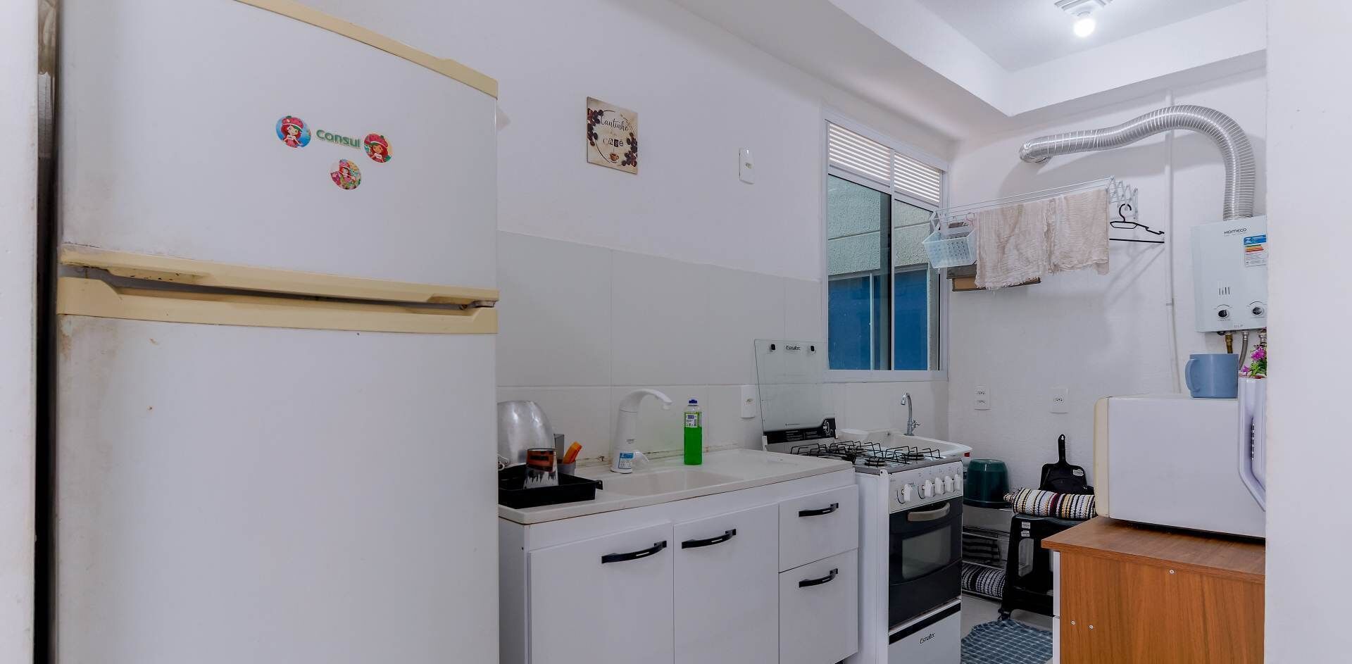 A compact kitchen with a refrigerator, stove, sink, and a window with blinds.
