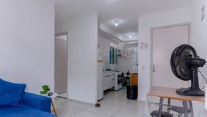 A modern living room with a blue sofa, a standing fan, and a kitchen area in the background.