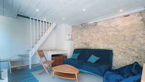 A modern living room with a blue sofa, a wooden chair, a small table, and a staircase with white railings.