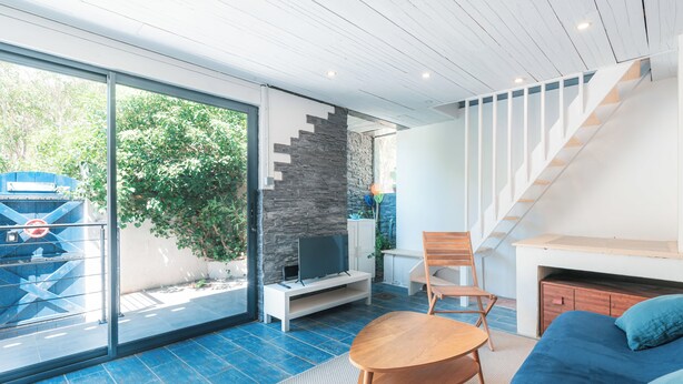 A modern living room with a blue sofa, a wooden coffee table, a TV on a white stand, and a stone wall.