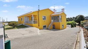 A yellow building with a balcony, a staircase, and a paved driveway.