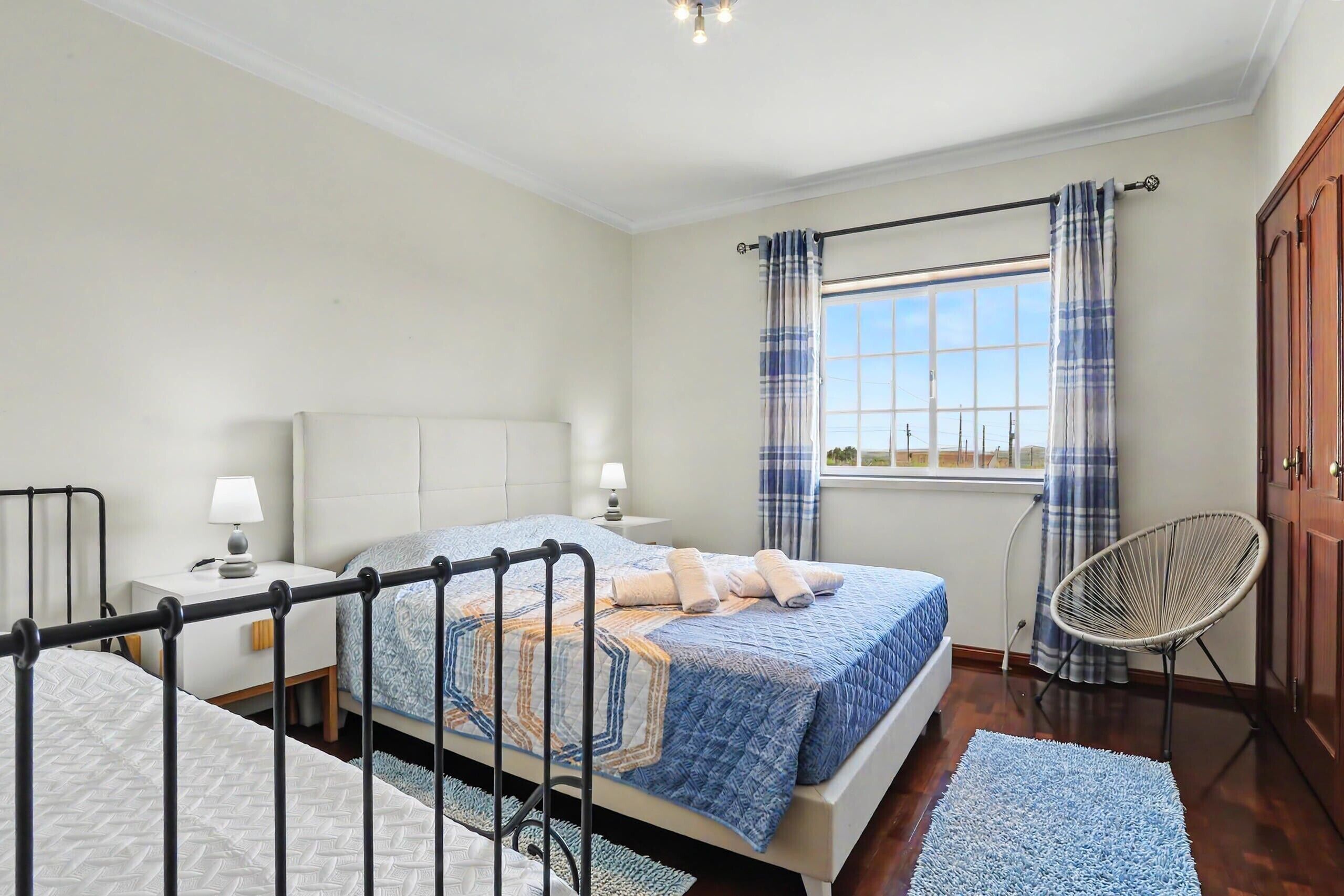 Une chambre à coucher avec un lit, des tables de chevet, une chaise, une fenêtre avec des rideaux et une vue.