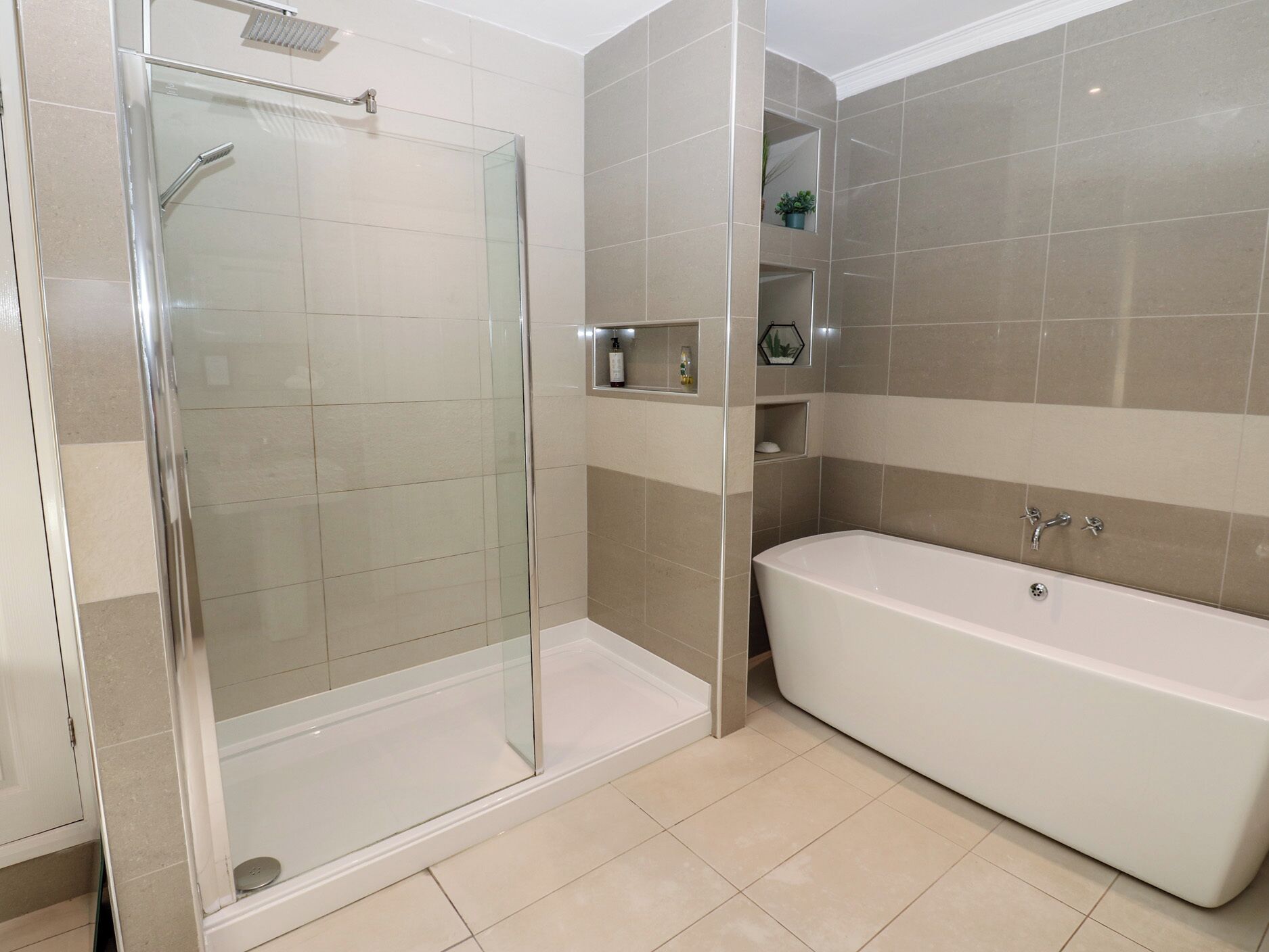 A modern bathroom with a glass-enclosed shower, a freestanding bathtub, and beige tiled walls.