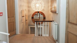 A hallway with a wooden door, a white railing, and a decorative light fixture. - Hampton House (St Bees)
