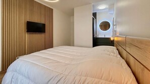 Ein modernes Schlafzimmer mit einem Bett, einem an einer Holzvertäfelung befestigten Fernseher und einer runden Leuchte darüber.
