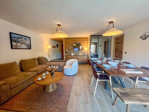 A modern living room with a sofa, coffee table, and dining area with chairs and a wooden table. - Wifi, 50m from resort center, 2nd floor, view resort, balcony, tv, ski locker, 98m², Les Gets (Les Gets)