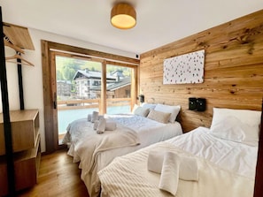 A hotel room with two beds, wooden walls, a large window, and a view of buildings. - Wifi, 50m from resort center, 2nd floor, view resort, balcony, tv, ski locker, 98m², Les Gets (Les Gets)