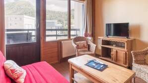 Una stanza accogliente con un'ampia finestra, un televisore su un mobile in legno, una poltrona in vimini e un divano rosso.