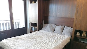 A bedroom with a bed, wooden headboard, built-in shelves, and a window. - 100m from ski slopes, 1st floor, view village, balcony, tv, 26m², Le Grand Bornand (Le Grand-Bornand)