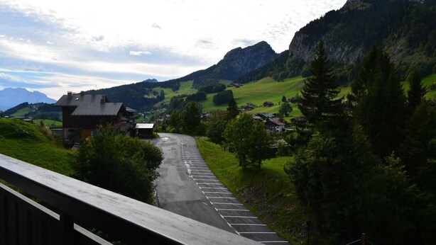 A rural road with a wooden fence, houses, and mountains in the background. - 100m from ski slopes, 1st floor, view village, balcony, tv, 26m², Le Grand Bornand (Le Grand-Bornand)
