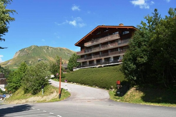 A multi-story building with balconies, located on a hillside with a mountain in the background.