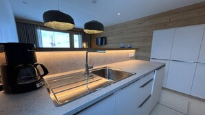 Una cucina moderna con lavello in acciaio inox, una macchina per il caffè e lampade a sospensione.