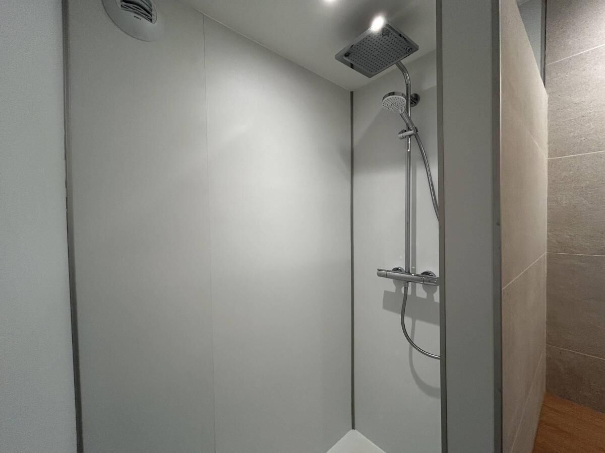 A modern shower enclosure with a handheld showerhead and a wall-mounted control panel.