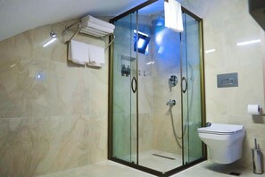 Casa de banho moderna com cabine de chuveiro em vidro, sanita e um porta-toalhas com toalhas dobradas.