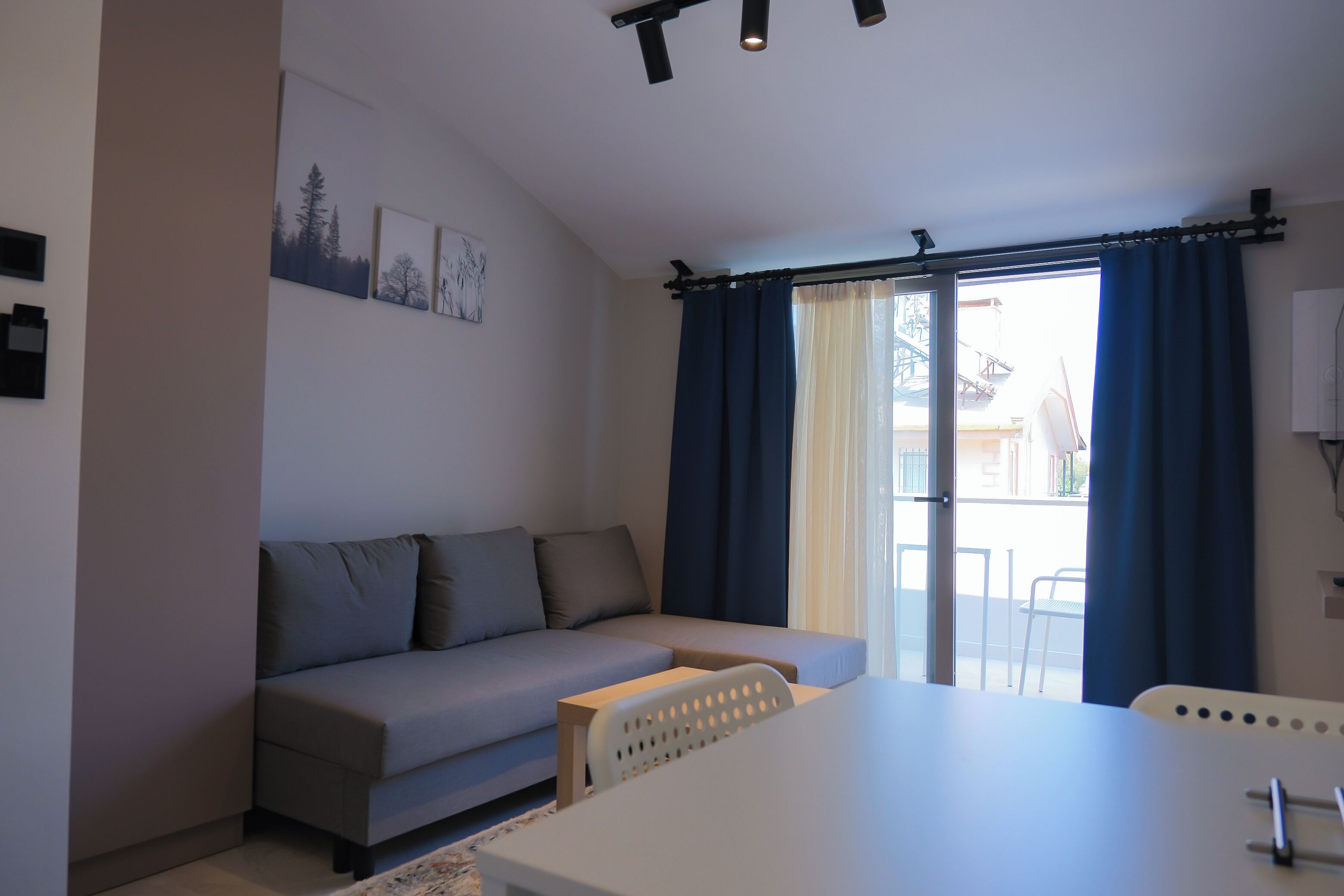 Una sala de estar moderna con un sofá gris, una mesa blanca y un amplio ventanal con cortinas azules.