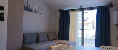 Una sala de estar moderna con un sofá gris, una mesa blanca y un amplio ventanal con cortinas azules.