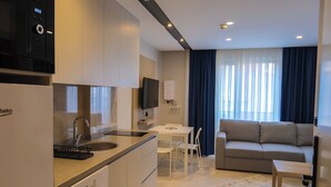 A modern kitchen with a built-in oven, a sink, and a dining area with a table and chairs. - Solmare Suites (Konyaalti)