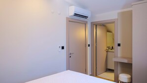 A modern hotel room with a bed, an air conditioning unit, a door, and a small stool. - Solmare Suites (Konyaalti)