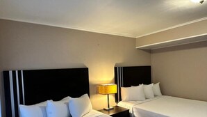 Hotellihuone, jossa on kaksi erillistä sänkyä, yöpöytä lampun kanssa ja pelkistetty seinä.