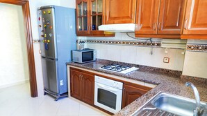 Een keuken met houten kastjes, een roestvrijstalen koelkast, een magnetron, een gasfornuis en een vaatwasser.