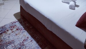 Een net opgemaakt bed met een witte matras en een opgerolde witte handdoek erop.