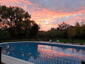 A swimming pool with a fence, surrounded by trees and a sunset sky. - Country House 'Monte Horta Da Velhinha' with Private Pool, Wi-Fi & Air Conditioning (Redondo)