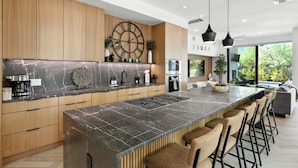 Une cuisine moderne dotée d’un grand îlot central, de meubles en bois et d’une grande fenêtre donnant sur un paysage verdoyant.