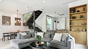 Un salon moderne avec un canapé d’angle gris, une table basse ronde et un escalier menant à l’étage supérieur.