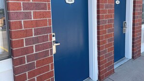 Deux portes bleues, portant les numéros 104 et 102, qui indiquent qu’il s’agit d’unités distinctes, sont adossées à un bâtiment en briques rouges.