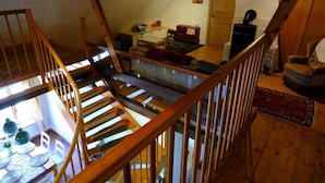 A wooden staircase leading to a loft bedroom with a bed, a desk, and a chair.
