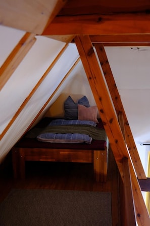 Un dormitorio cálido y acogedor en el ático, con cama de madera, almohadas y suelo cubierto de alfombra.