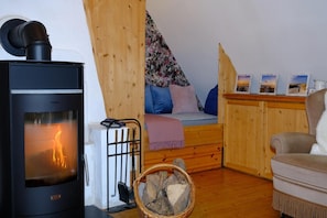 Una habitación acogedora con una estufa de leña, una cama con colcha estampada y una mesita con marcos de fotos.