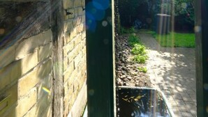 A narrow alleyway with a brick wall on one side and a garden on the other.