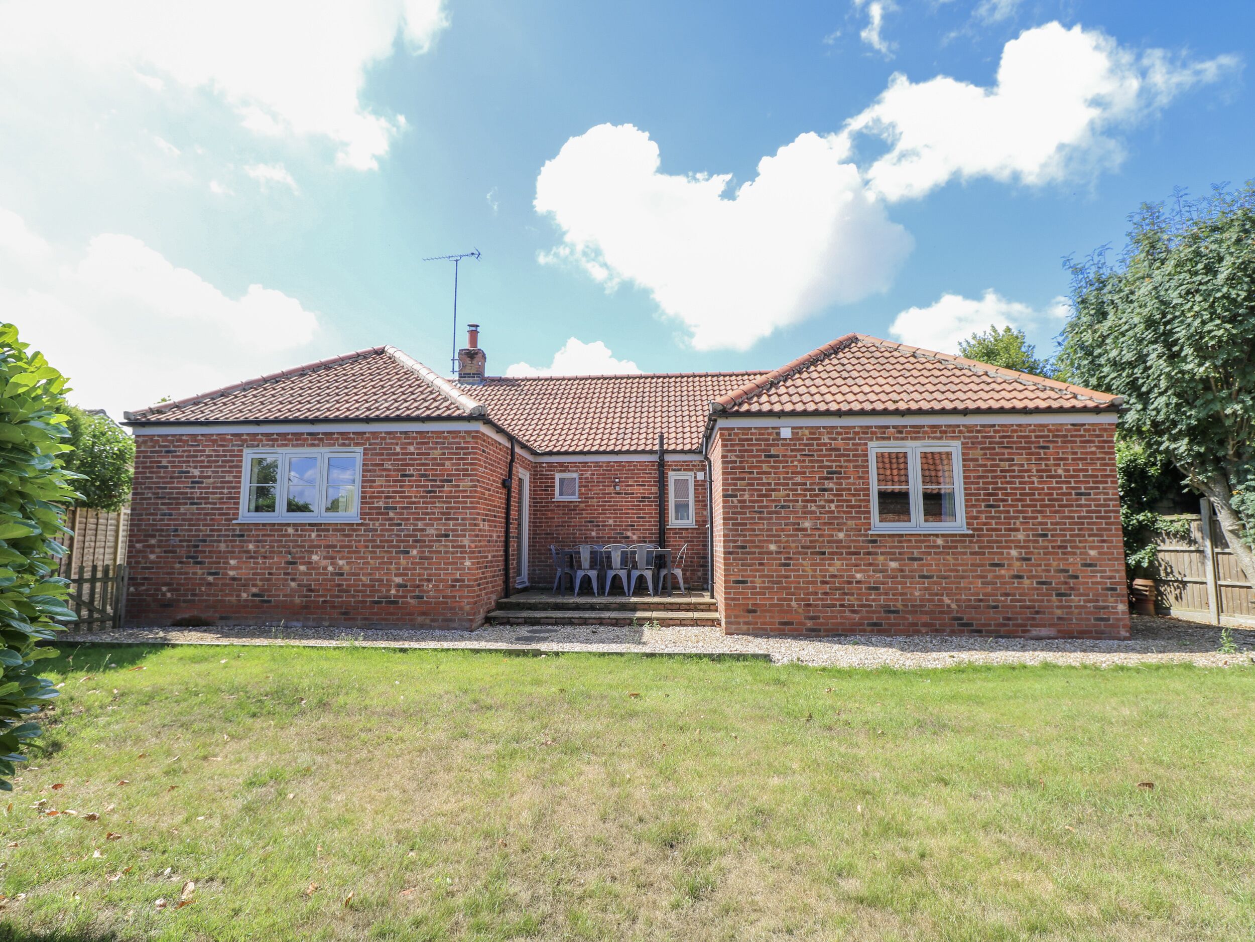 A two-story brick house with a tiled roof, a chimney, and a small front porch with chairs.