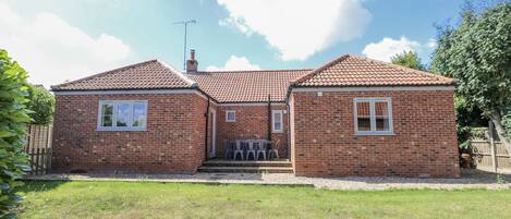 A two-story brick house with a tiled roof, a chimney, and a small front porch with chairs.