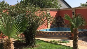 Une cour avec une piscine carrelée, des palmiers et un bâtiment orné d’une bordure de carreaux.