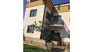 Un bâtiment à deux étages doté d’un balcon, d’un petit jardin et d’un escalier menant à l’entrée.
