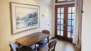 A dining area with a wooden table and chairs, a framed painting on the wall, and a large window with curtains. - Private & Serene 2BR with Amazing Lake Sammamish Views (Sammamish)