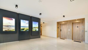 A modern lobby with a clean, tiled floor, three large wall-mounted screens displaying scenic views, and a wooden elevator with a door.
