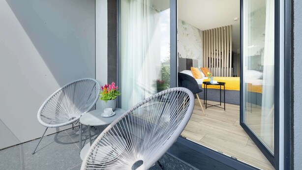 A balcony with two white wire chairs, a small table, and a potted plant.