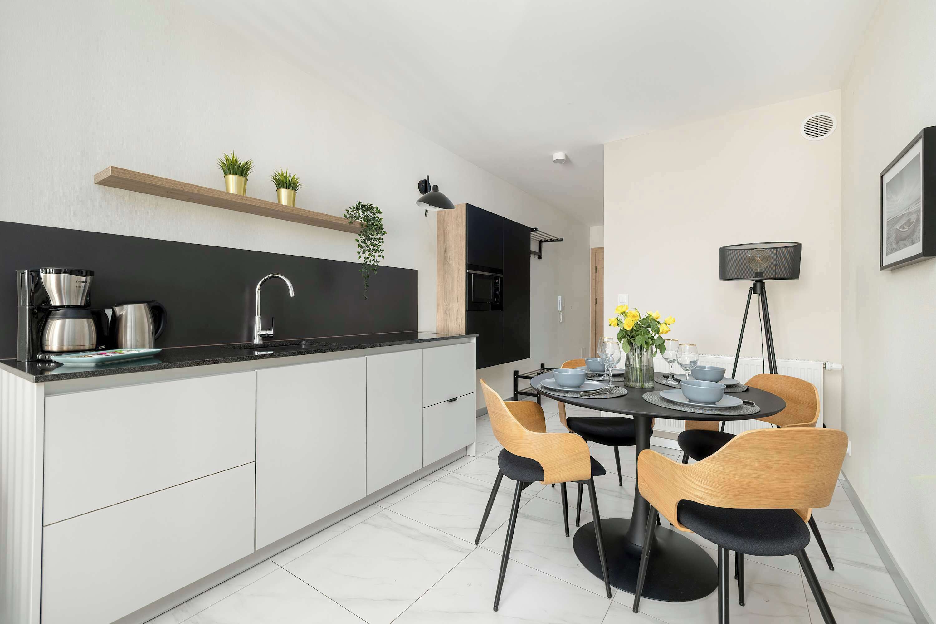 A modern kitchen with a black countertop, white cabinets, and a dining area with a round table and chairs.