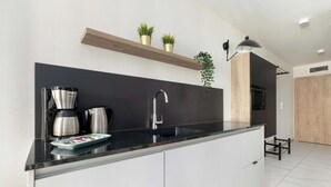 A modern kitchen with a black countertop, stainless steel appliances, and white cabinets. There is a wooden shelf above the sink with potted plants.