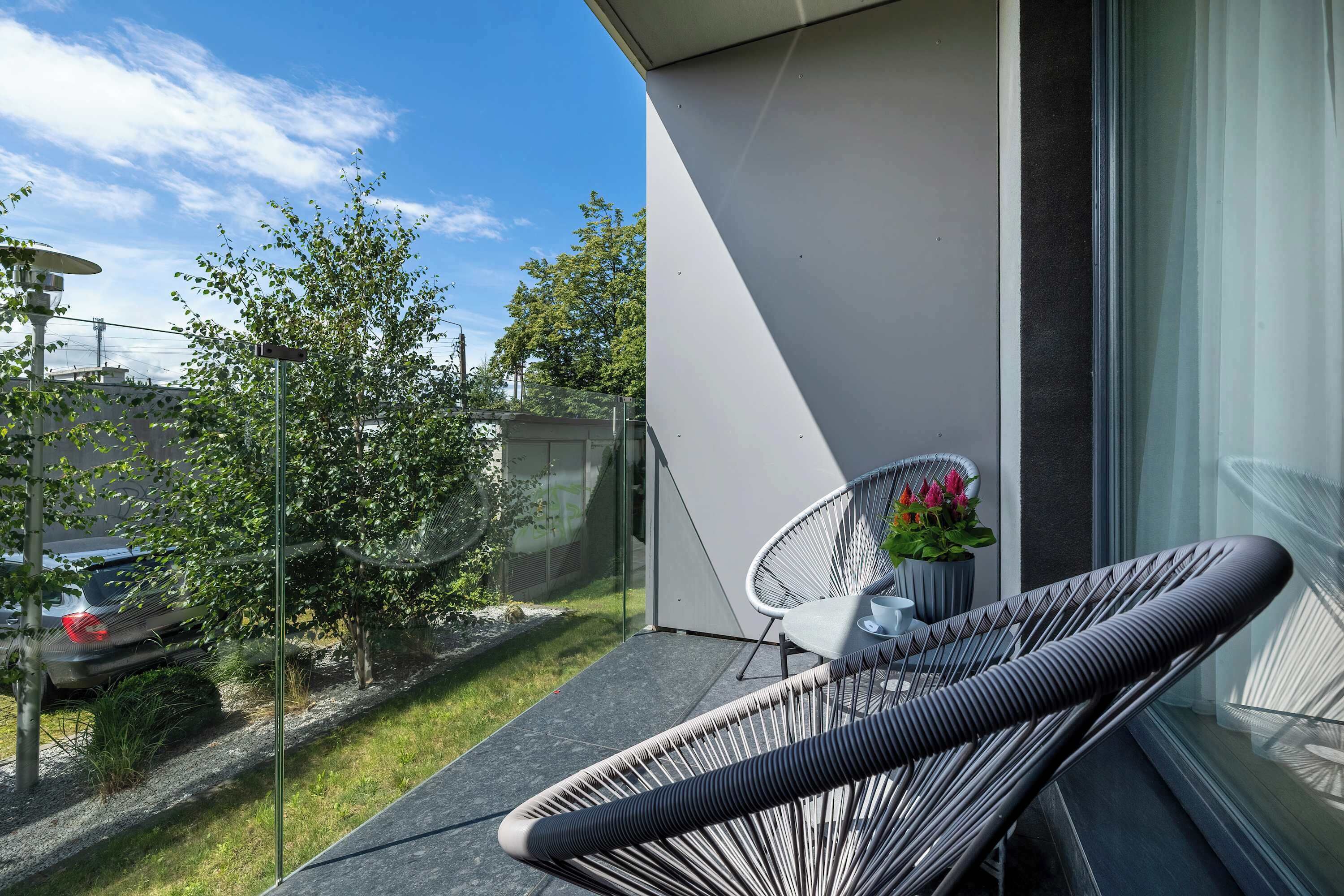 Ein Balkon mit Korbstuhl, Topfpflanze und Glastür zum Garten.